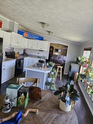 kitchen with a textured ceiling, sink, black appliances, white cabinetry, and an island with sink