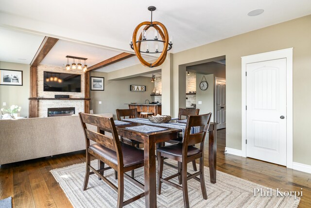 250 Shore Dr, Wayland, MI 49348 - dining room featuring a chandelier, wood-type flooring, a large fireplace, beamed ceiling, and baseboards
