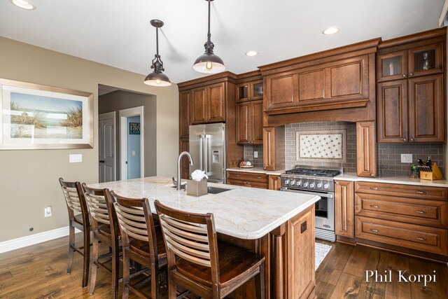 250 Shore Dr, Wayland, MI 49348 - kitchen featuring high end appliances, dark wood-type flooring, baseboards, a center island with sink, and tasteful backsplash