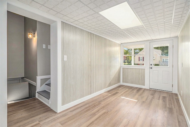 interior space with hardwood / wood-style floors, a drop ceiling, and wooden walls