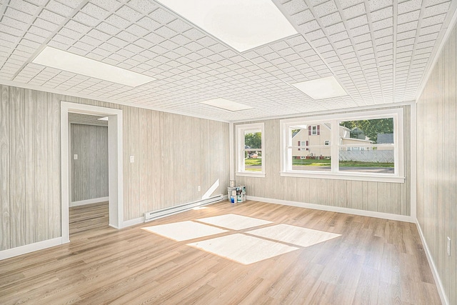 unfurnished room with wooden walls, light hardwood / wood-style floors, and a baseboard radiator