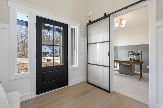 doorway to outside with a barn door, light wood-style flooring, and wainscoting