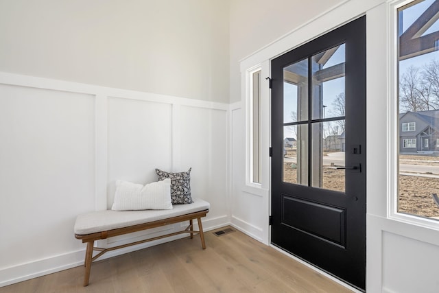 interior space with a decorative wall, light wood-type flooring, visible vents, and a wainscoted wall