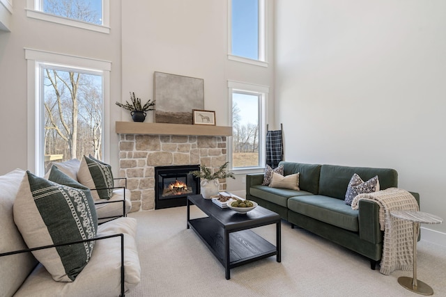 living room featuring a stone fireplace, carpet flooring, a healthy amount of sunlight, and a towering ceiling