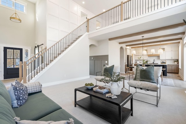 living area with baseboards, beam ceiling, light carpet, a towering ceiling, and arched walkways