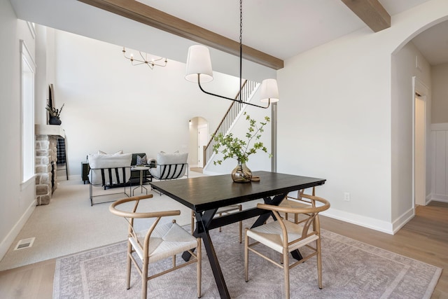 dining space with an inviting chandelier, beamed ceiling, wood finished floors, and arched walkways