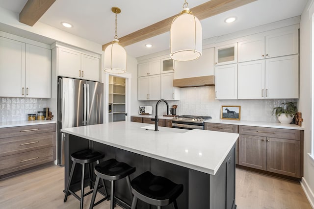 kitchen featuring a kitchen bar, beam ceiling, light wood-type flooring, and stainless steel appliances