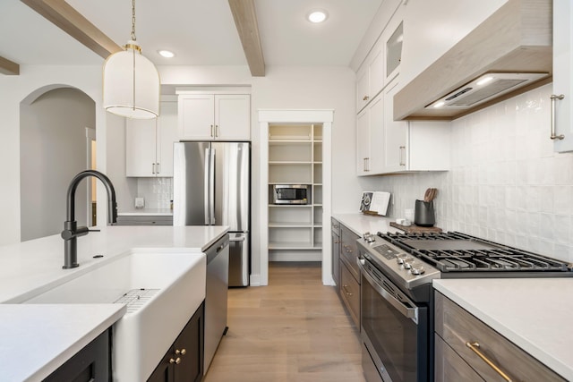 kitchen featuring premium range hood, decorative light fixtures, beam ceiling, appliances with stainless steel finishes, and white cabinetry