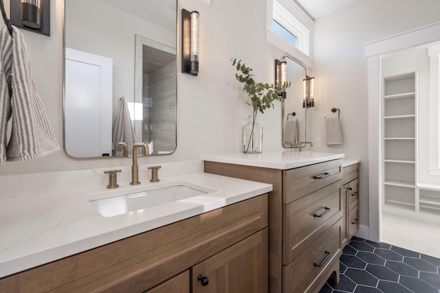 bathroom featuring tile patterned flooring, a walk in closet, two vanities, and a sink