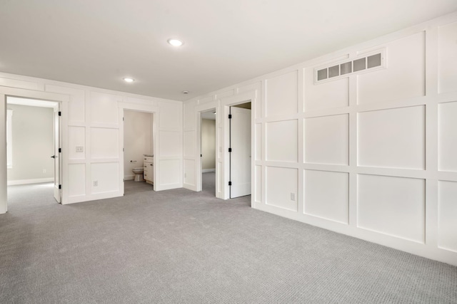 unfurnished bedroom with a decorative wall, recessed lighting, visible vents, and carpet floors