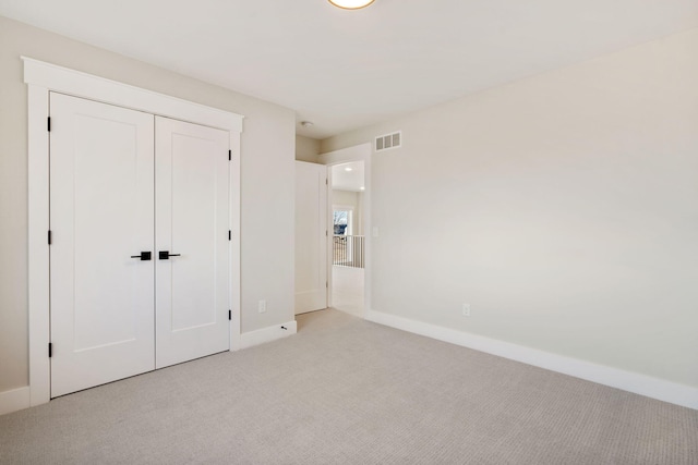 unfurnished bedroom featuring light colored carpet, visible vents, a closet, and baseboards