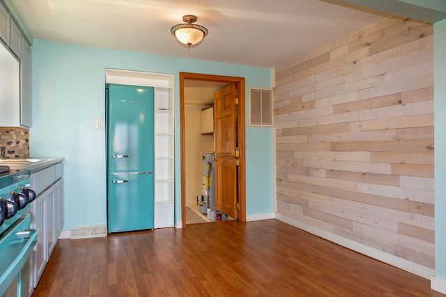 interior space with wood walls, water heater, stainless steel appliances, and dark wood-type flooring