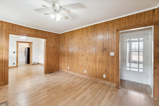 empty room with ceiling fan, wooden walls, crown molding, and light wood-type flooring