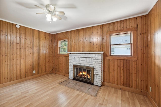 unfurnished living room featuring crown molding, hardwood / wood-style floors, a brick fireplace, ceiling fan, and wood walls