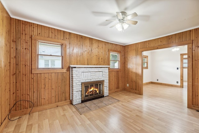 unfurnished living room featuring crown molding, ceiling fan, a fireplace, wood walls, and light hardwood / wood-style floors