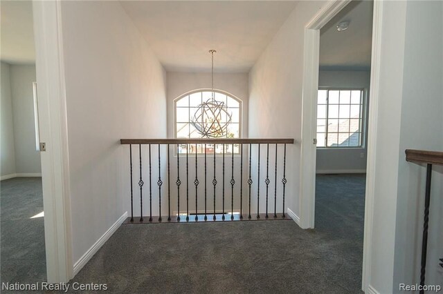 hallway featuring dark carpet and a notable chandelier