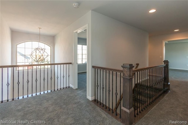 corridor with a chandelier, dark carpet, and a wealth of natural light