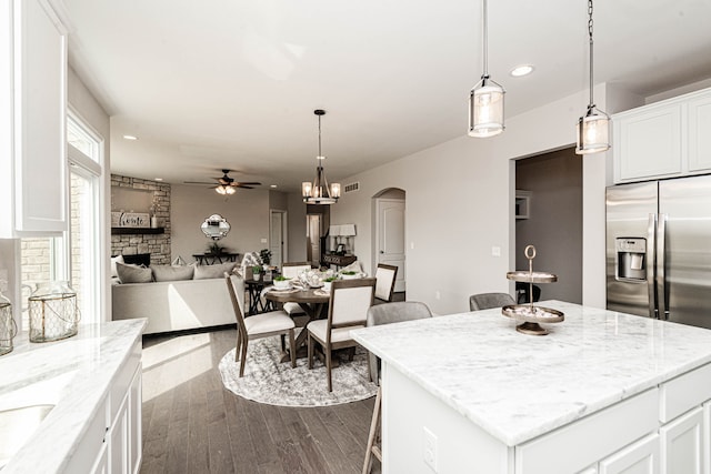 kitchen with stainless steel fridge, light stone counters, a kitchen island, dark hardwood / wood-style floors, and white cabinetry