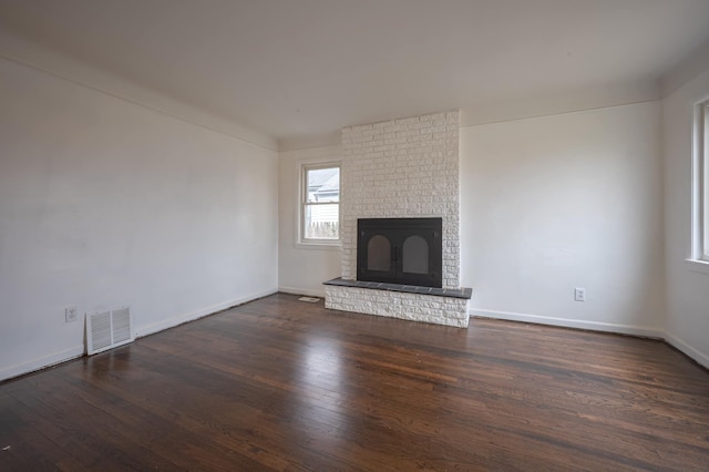 unfurnished living room with a brick fireplace and dark wood-type flooring