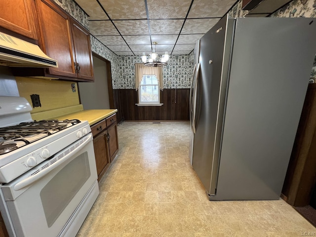 kitchen with an inviting chandelier, stainless steel fridge, wooden walls, and white range with gas stovetop