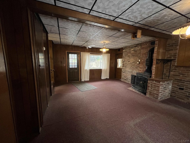 unfurnished living room with dark carpet, a wood stove, and wood walls