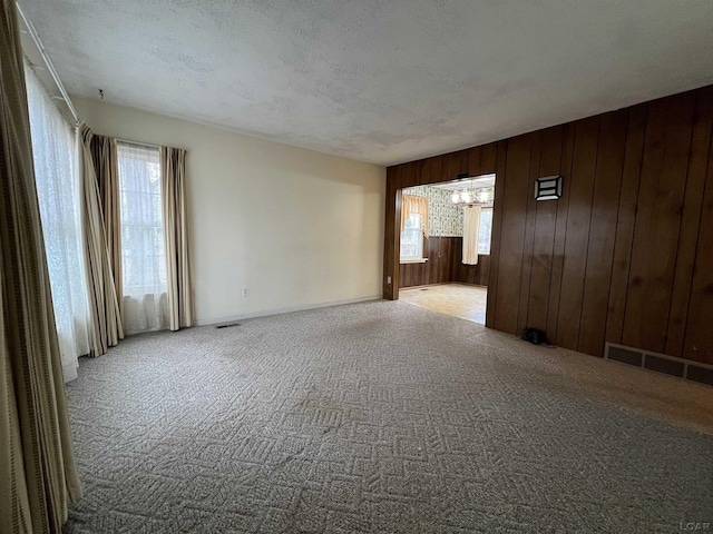 empty room featuring a textured ceiling, light carpet, and wood walls