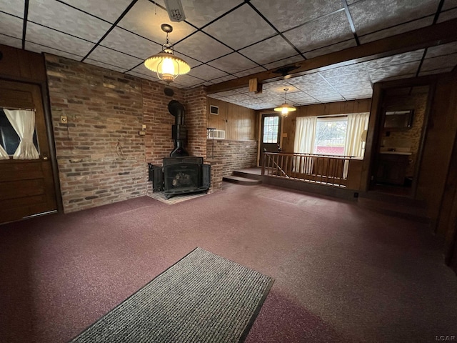 unfurnished living room with brick wall, carpet flooring, a wood stove, and wooden walls