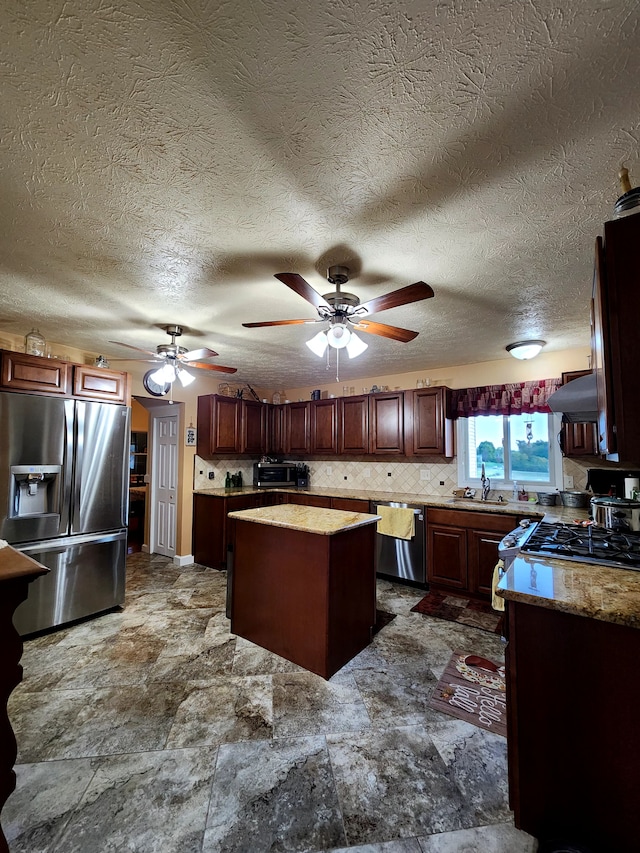 kitchen featuring sink, range hood, a textured ceiling, a kitchen island, and appliances with stainless steel finishes