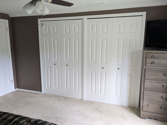 unfurnished bedroom featuring a textured ceiling, ceiling fan, carpet floors, and two closets