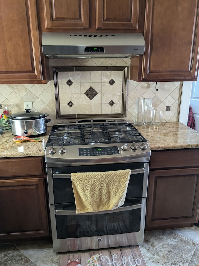 kitchen with decorative backsplash, light stone countertops, double oven range, and range hood