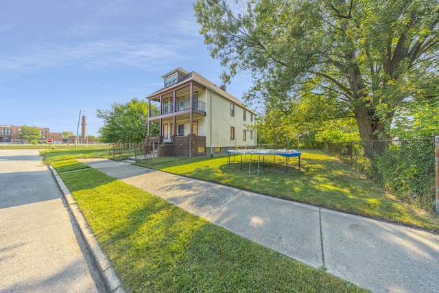 view of front of house featuring a balcony, a trampoline, and a front lawn