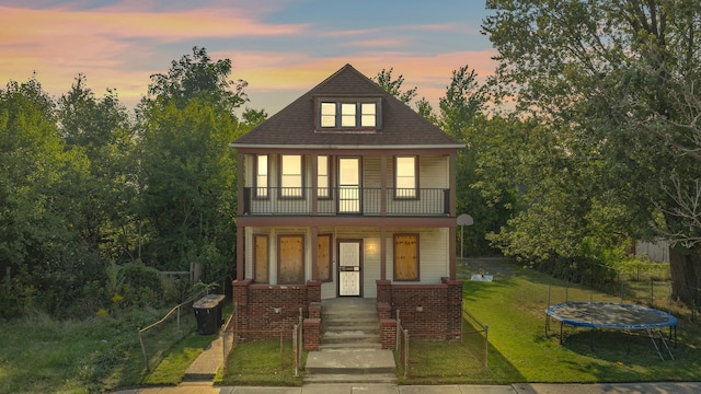 view of front facade with a trampoline, a porch, a balcony, a yard, and central AC unit