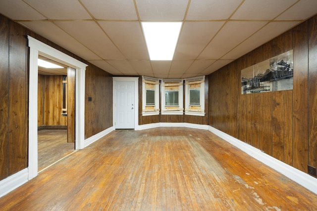 empty room with wooden walls, a drop ceiling, and wood-type flooring