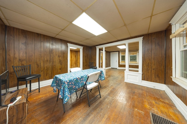 dining room with hardwood / wood-style floors, a paneled ceiling, decorative columns, and wood walls