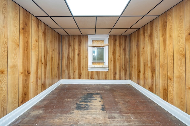 basement featuring hardwood / wood-style floors, a drop ceiling, and wooden walls