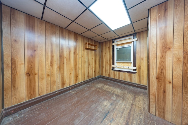 empty room with a paneled ceiling, wood walls, and dark wood-type flooring