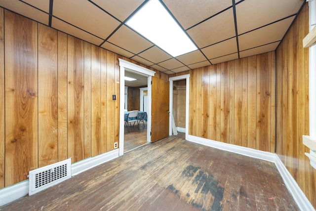 interior space featuring hardwood / wood-style floors, a drop ceiling, and wooden walls