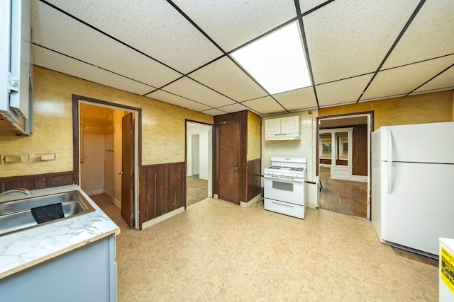 kitchen featuring wooden walls, a drop ceiling, white appliances, and sink