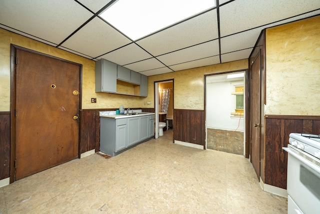 kitchen featuring sink, wood walls, gray cabinets, a paneled ceiling, and white gas range oven