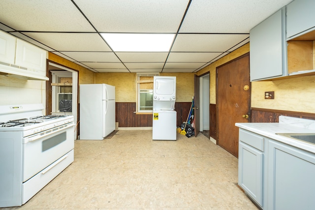 kitchen with sink, wood walls, stacked washer and dryer, white appliances, and a paneled ceiling