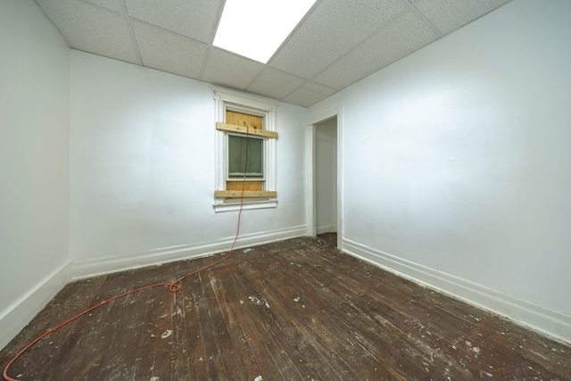 empty room with dark hardwood / wood-style flooring and a drop ceiling