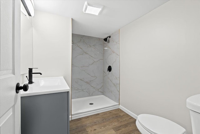 bathroom with a tile shower, vanity, wood-type flooring, and toilet