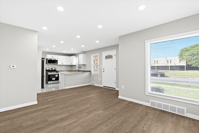 kitchen with white cabinets, sink, kitchen peninsula, appliances with stainless steel finishes, and wood-type flooring