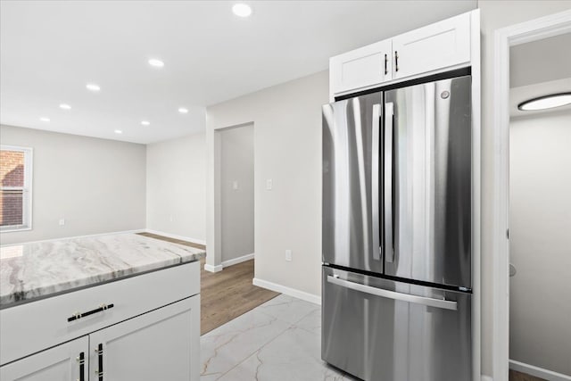 kitchen with stainless steel fridge, white cabinets, and light stone counters