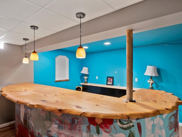 bar with wood-type flooring, a drop ceiling, hanging light fixtures, and butcher block counters