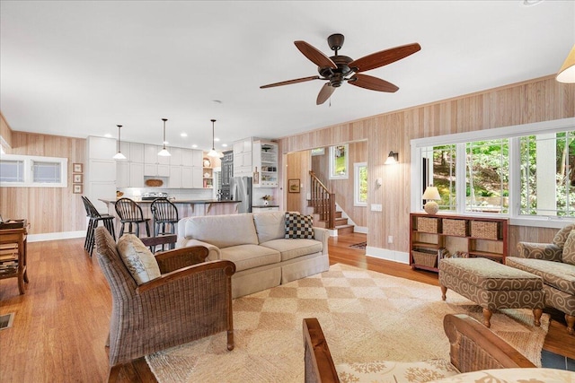 876 S Beach, Pentwater, MI 49449 - living area featuring baseboards, wood walls, light wood finished floors, a ceiling fan, and stairs