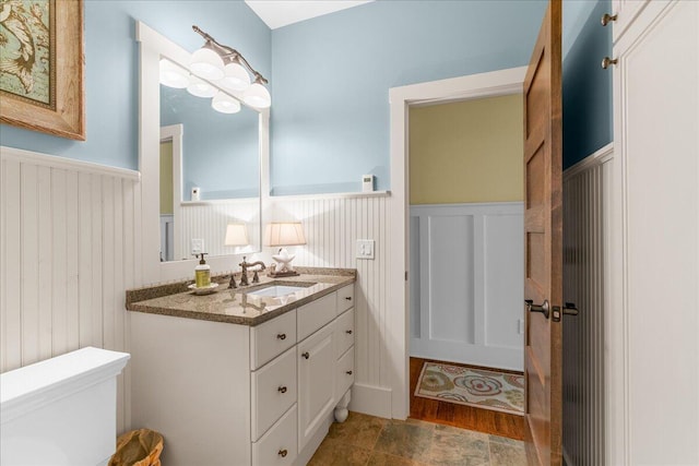 876 S Beach, Pentwater, MI 49449 - bathroom with wainscoting, toilet, vanity, a decorative wall, and stone finish floors
