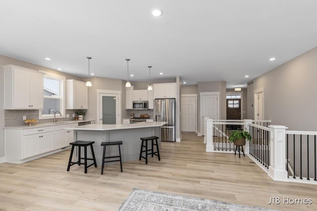 kitchen featuring a center island, light hardwood / wood-style floors, decorative light fixtures, and appliances with stainless steel finishes