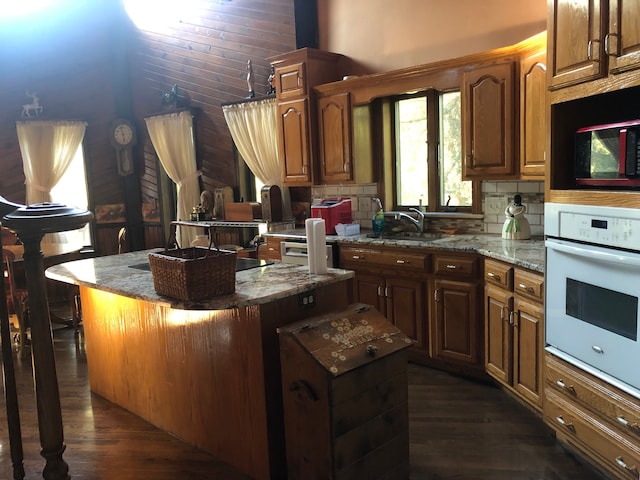 kitchen with white oven, dark wood-type flooring, sink, stone countertops, and a kitchen island