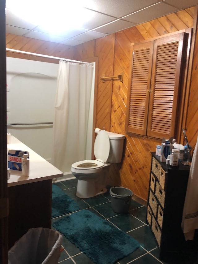 bathroom with tile patterned flooring, toilet, walk in shower, and wooden walls